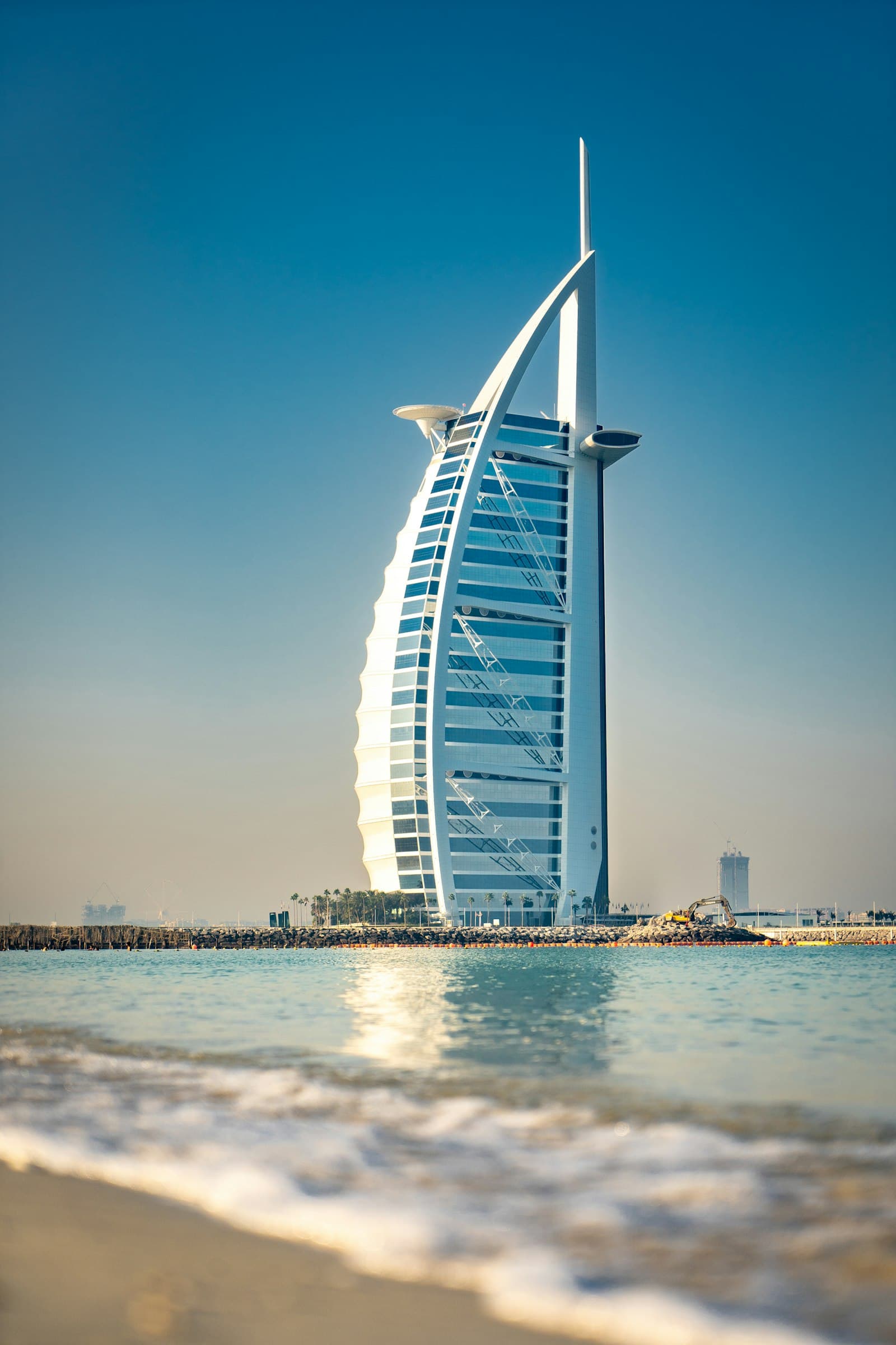 White-sand Dubai beach with gentle surf and an iconic sail-shaped tower on the horizon